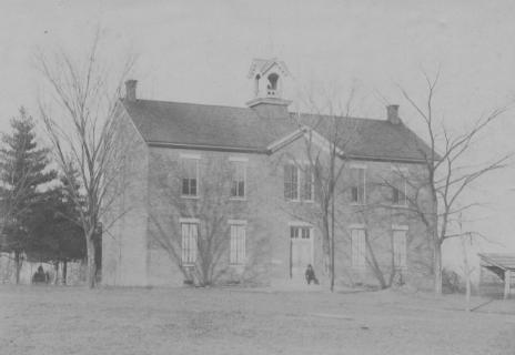 Old two-story building with a bell tower and bare trees.