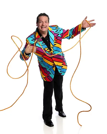 A man in a colorful, patterned suit playfully holds a rope, smiling at the camera against a white background.
