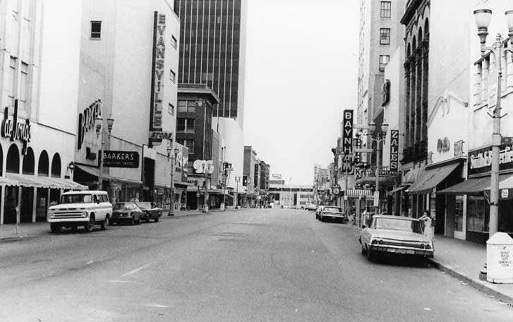 Vintage street scene with old cars, classic signage, and buildings.