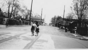 Black and white photo of two children walking down a street with houses and utility poles.