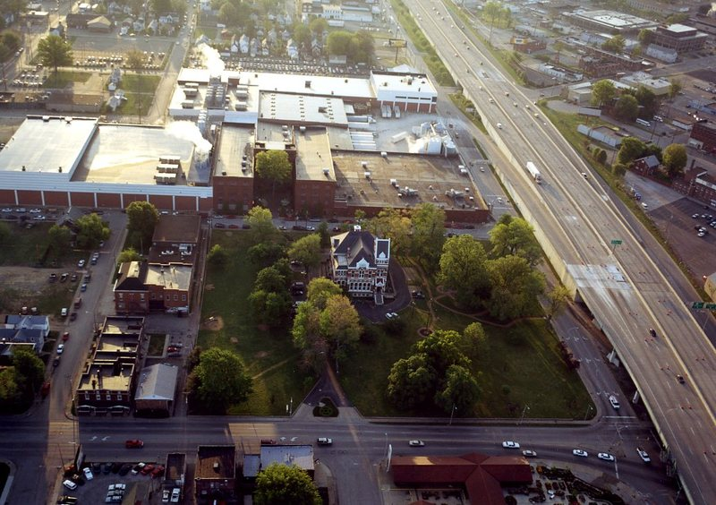 Aerial view of a Victorian-style house next to a highway and urban area at dusk.