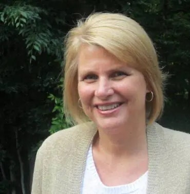 A smiling woman with short blond hair outdoors.