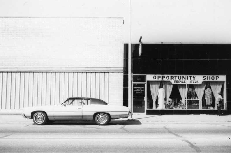 Vintage car parked in front of a thrift store called "Opportunity Shop."