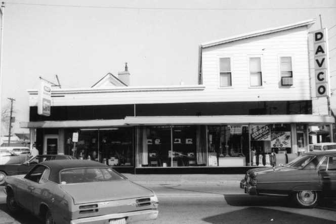 Vintage street scene with two cars parked outside a shop labeled "DAVCO." Black and white photo.