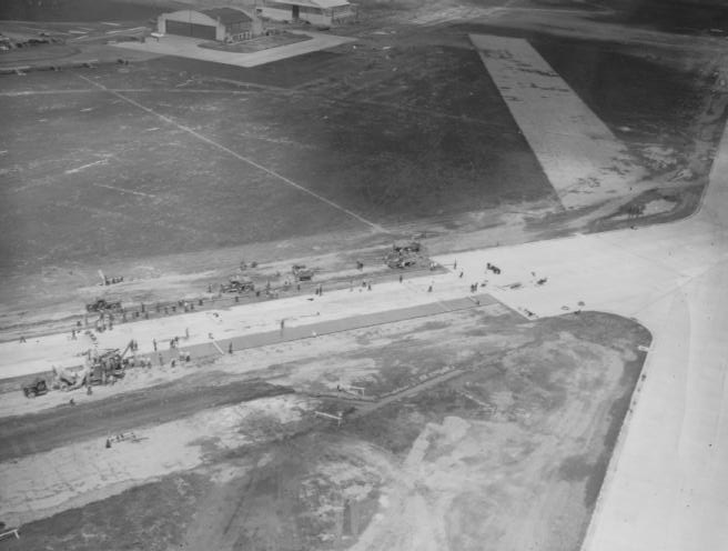 An aerial view of an airfield under construction with several buildings and vehicles.