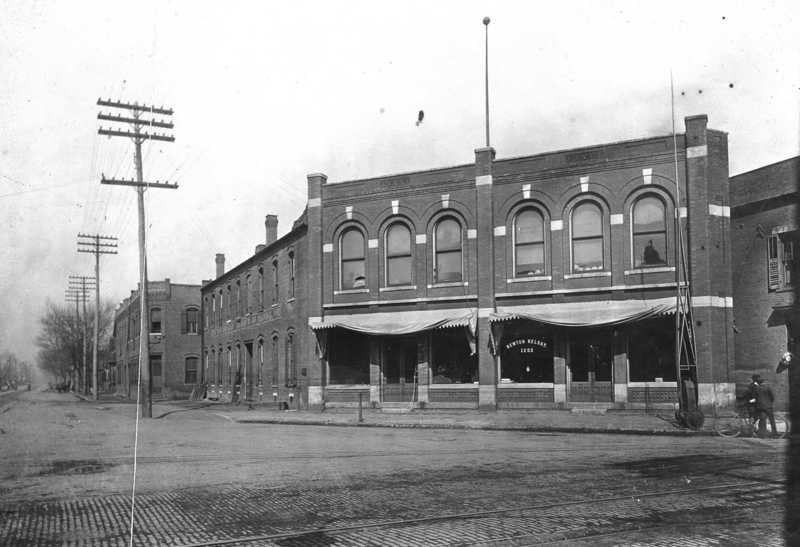 Historic street view with brick buildings, cobblestone road, and early telephone poles.