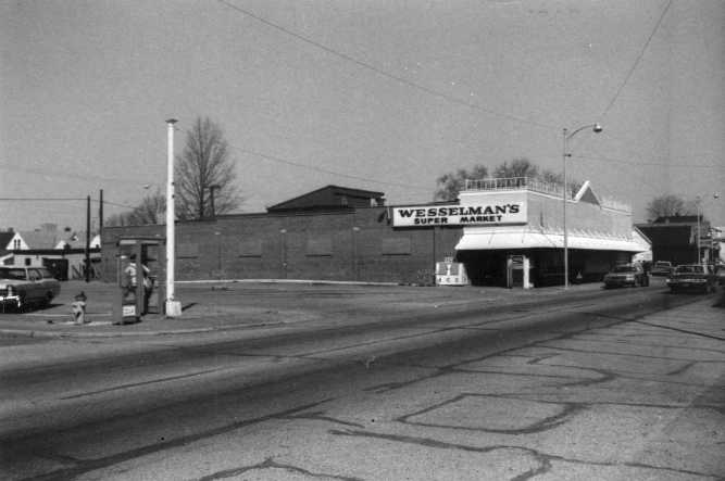 A black and white photo of a street with "Wesselman's Super Market," a power pole, and a clear sky.