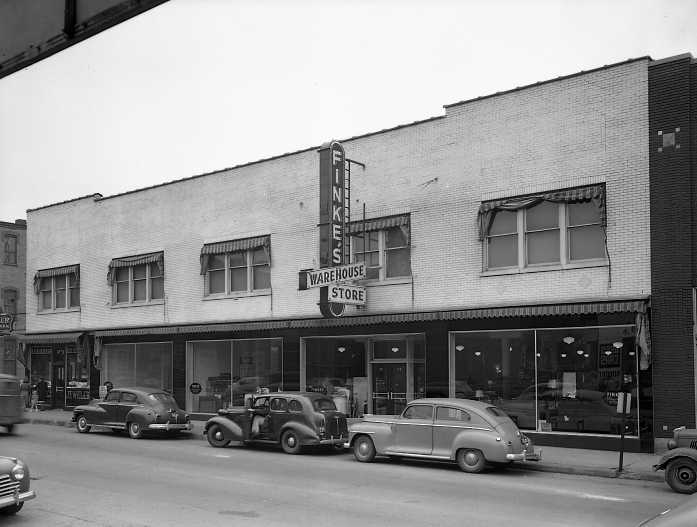 Black and white photo of a vintage street scene with old cars and a building with a sign "FINK'S WAREHOUSE STORE."