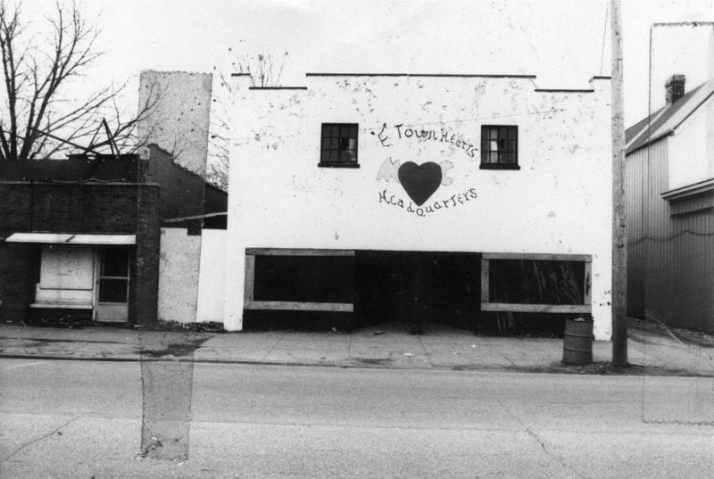 Black and white photo of a dilapidated building with graffiti reading "E-Town Rats Headquarters."