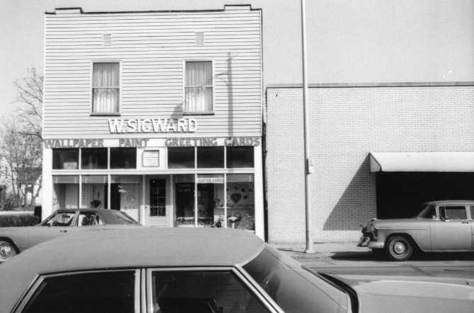 Black and white photo of vintage cars parked outside a building with a sign "WESTWARD."