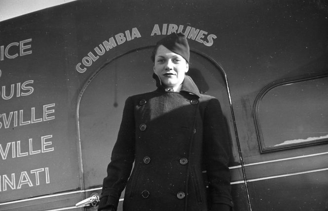 A woman standing by a plane with "Columbia Airlines" written above. Black and white photo.