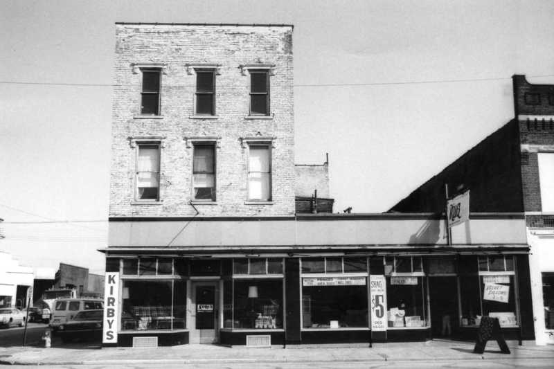 A black and white photo of a vintage storefront with signs "KIRBY'S" and "DRUG."