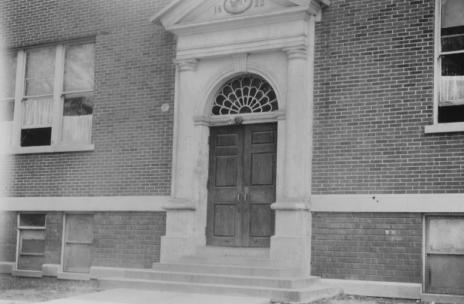 Vintage photo of a building façade with an ornate doorway and brick walls.