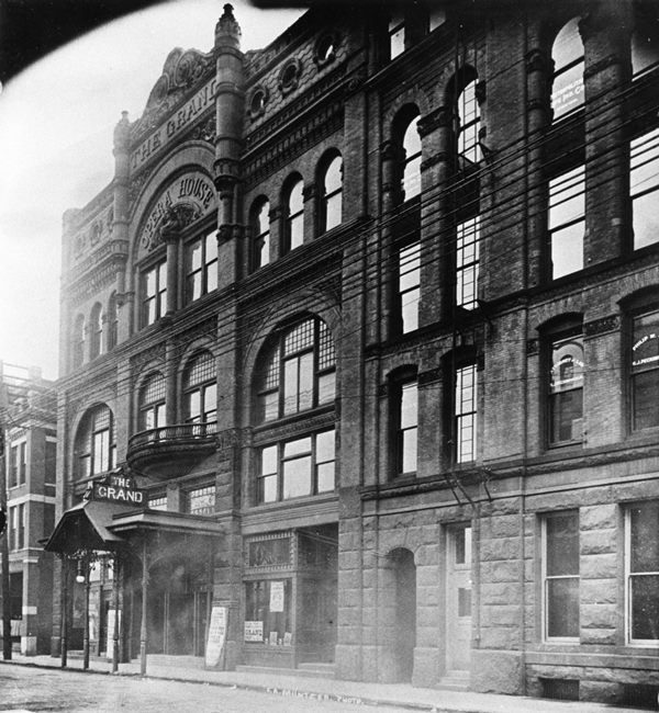 An old black-and-white photo of a historic building with "THE GRAND" sign, likely a theater or opera house.