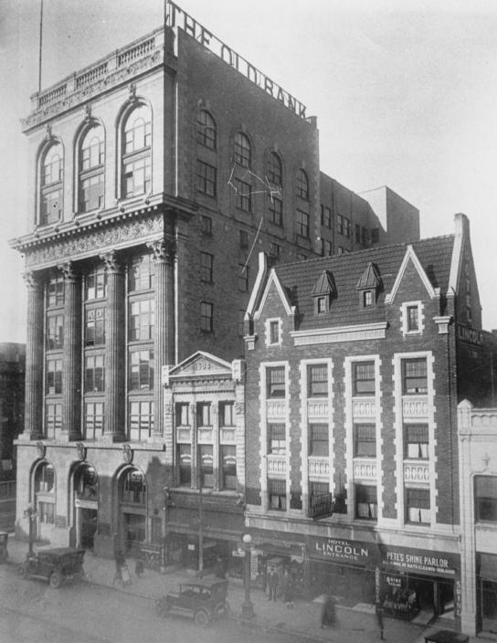 Historic black-and-white photo of early 20th-century buildings with vintage cars and pedestrians.