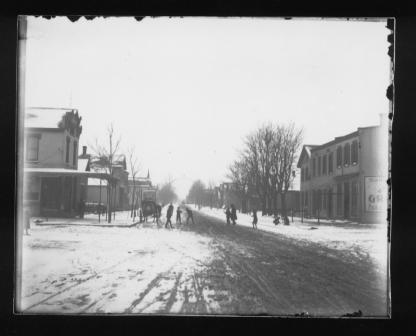 Vintage snowy street scene with people, horse-drawn carriage, and buildings.