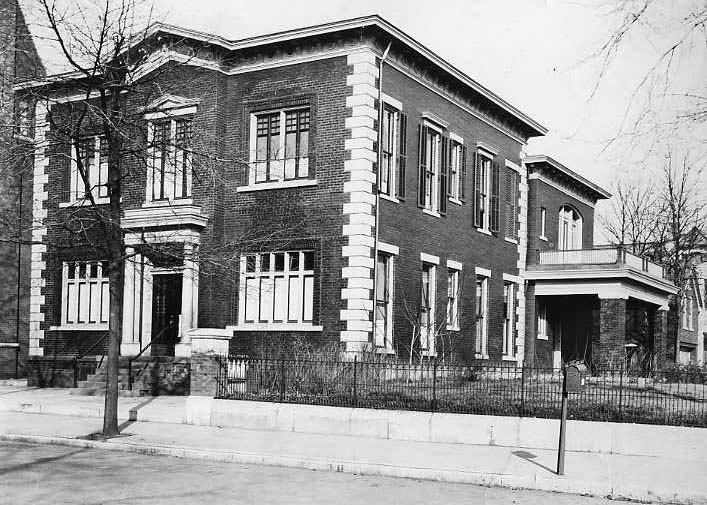 Vintage photo of a brick building with white trim, possibly an old school or municipal structure, no people visible.