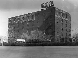 Black and white photo of an old building with "Coca-Cola" sign on top.