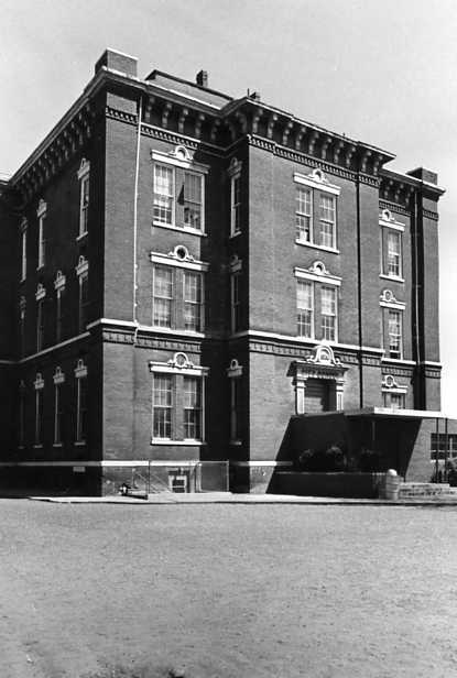 A black and white photo of a classical brick building, with large windows and a clear sky.