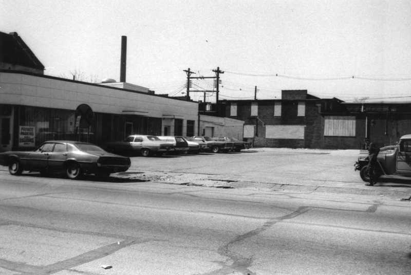 Vintage street view with old cars parked outside buildings, clear sky, power lines above.