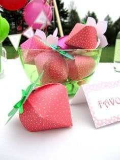 Pink paper favor boxes shaped like strawberries in a glass bowl, possibly for a party or wedding.