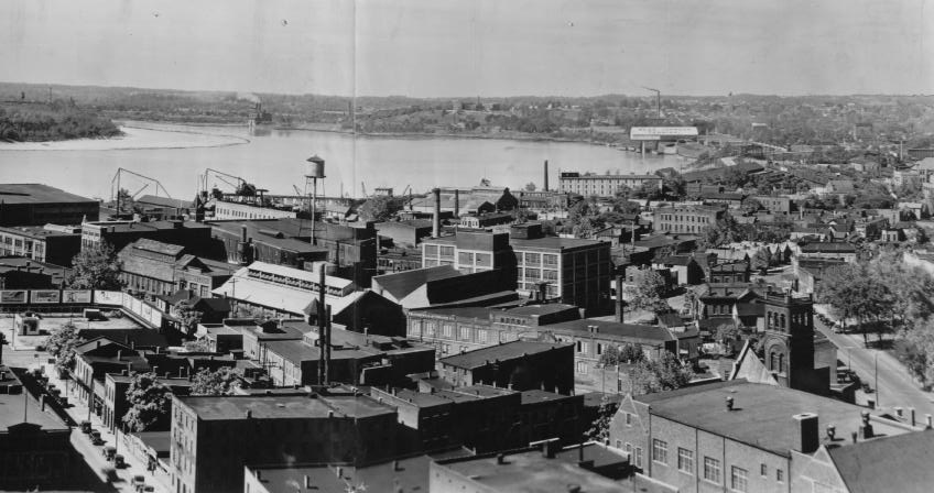 Historic aerial view of a cityscape with buildings, streets, and a river in the background.