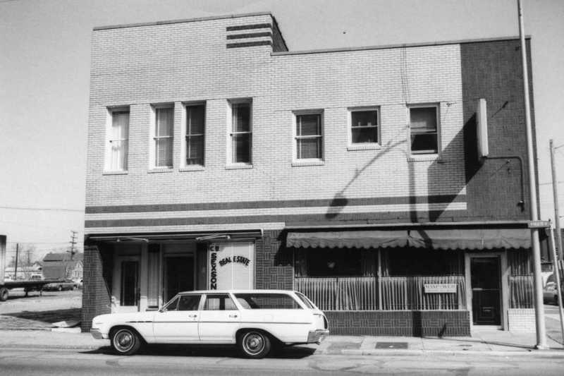 Black and white photo of an old building with a station wagon car parked in front.