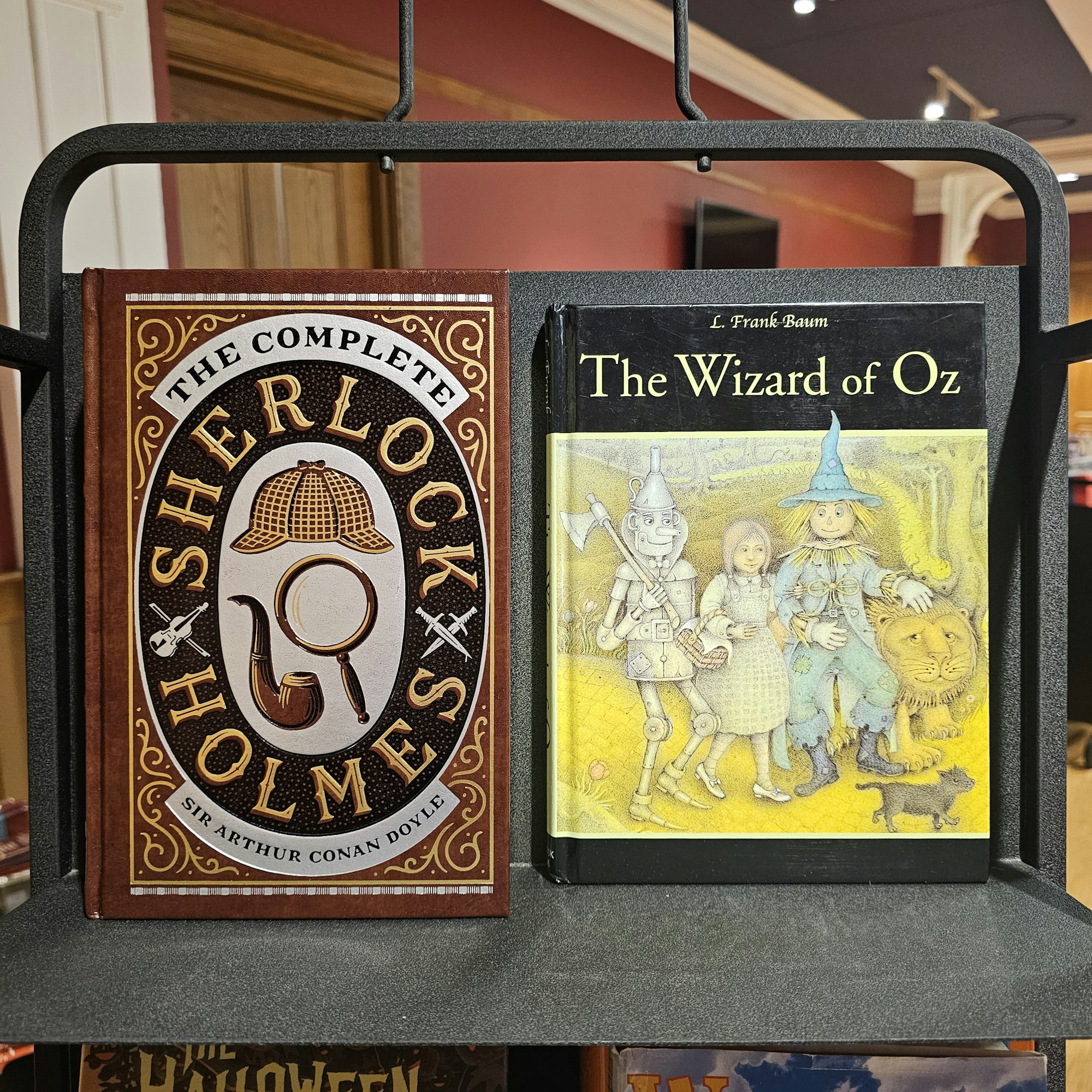 Two books: "The Wizard of Oz" on top, "The Complete Sherlock Holmes" below, displayed on a book rack.