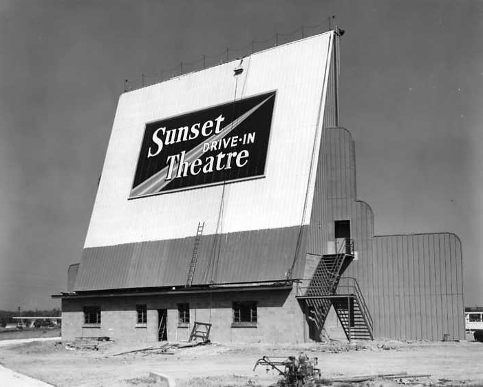 Black and white photo of the "Sunset Drive-In Theatre" large screen structure with stairs on the side.