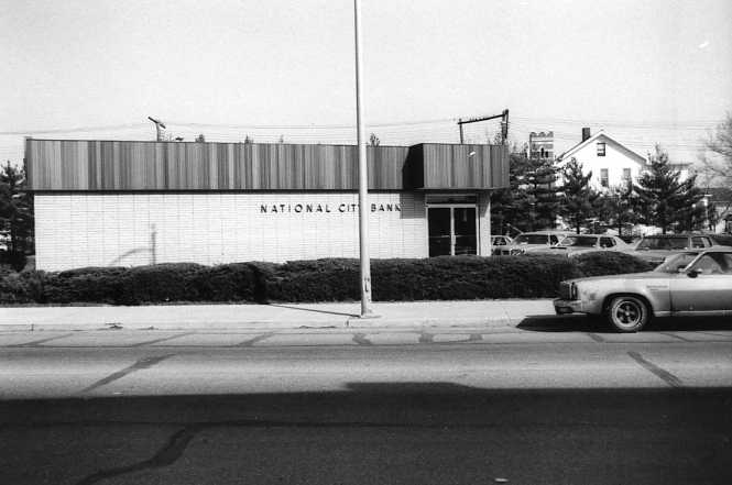 A bank building and a vintage car parked in front.