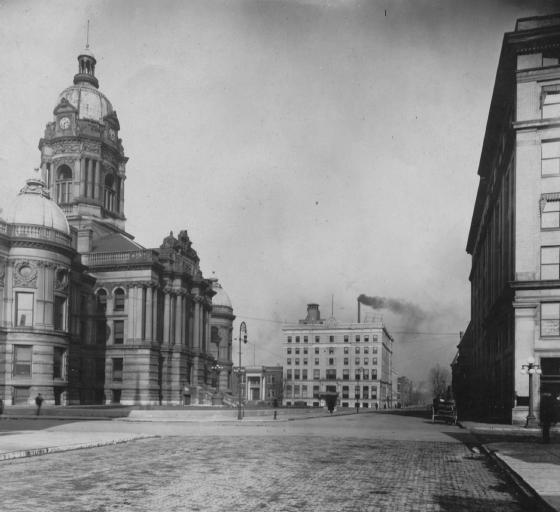 Historic city street with grand buildings, cobblestone road, and a person. Vintage photo aesthetic.