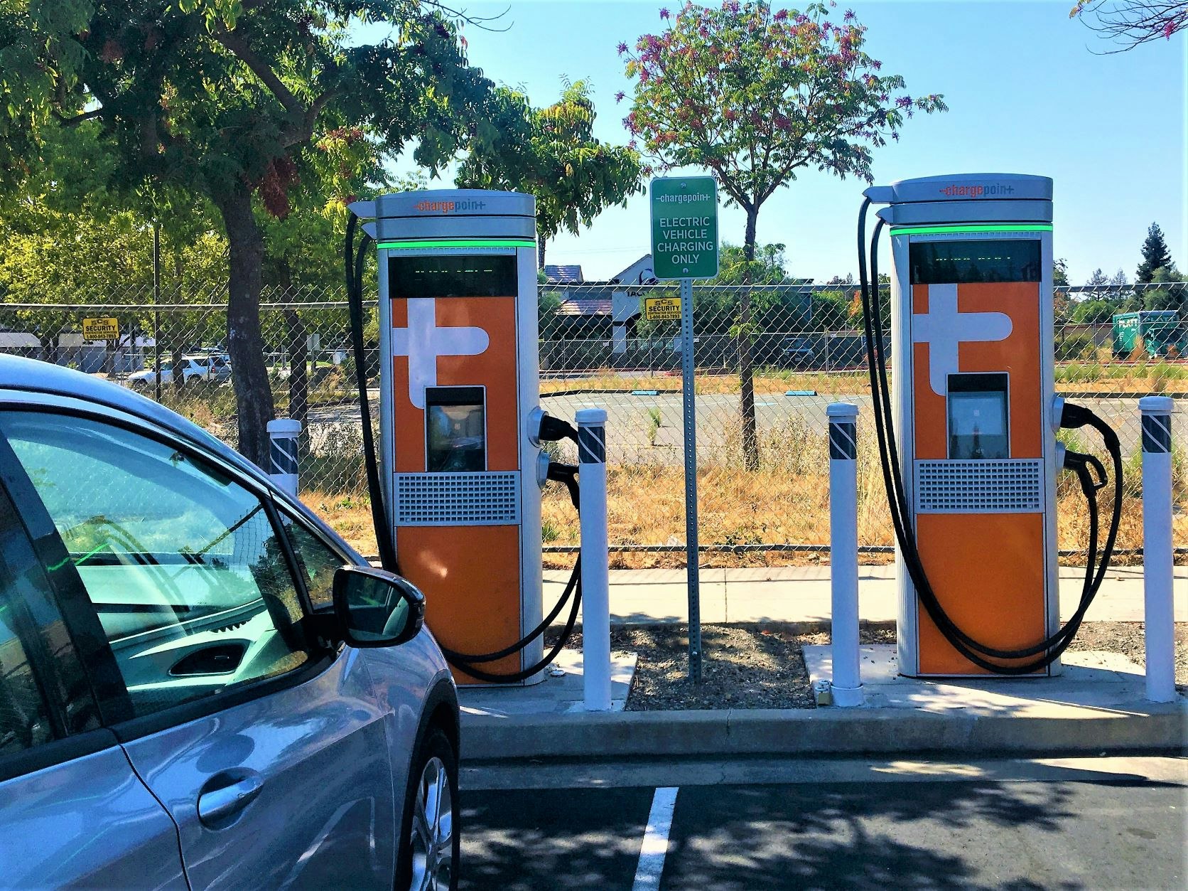 The image shows two electric vehicle charging stations with a nearby sign indicating "Electric Vehicle Charging Only."