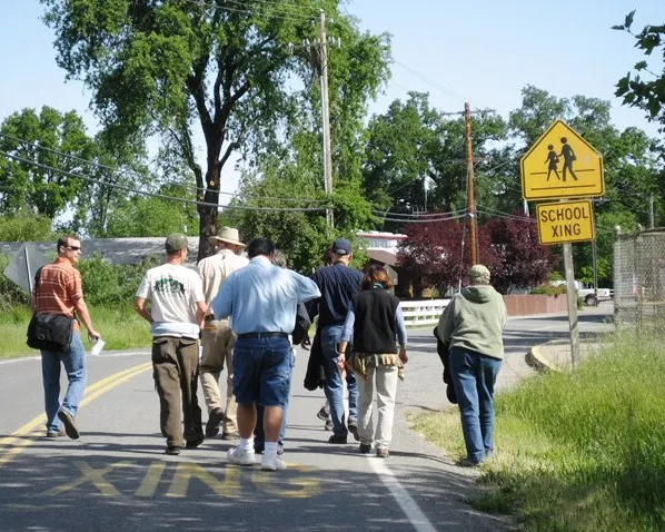 A group of people walking down a road near a school crossing sign on a clear day.