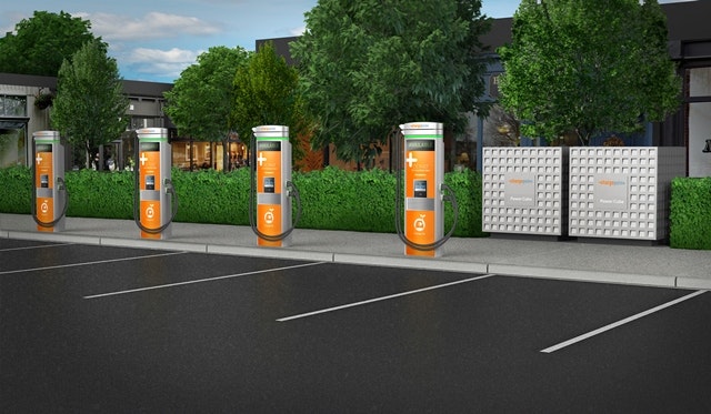 The image features multiple electric vehicle charging stations in a well-maintained parking lot with greenery and a modern building in the background.