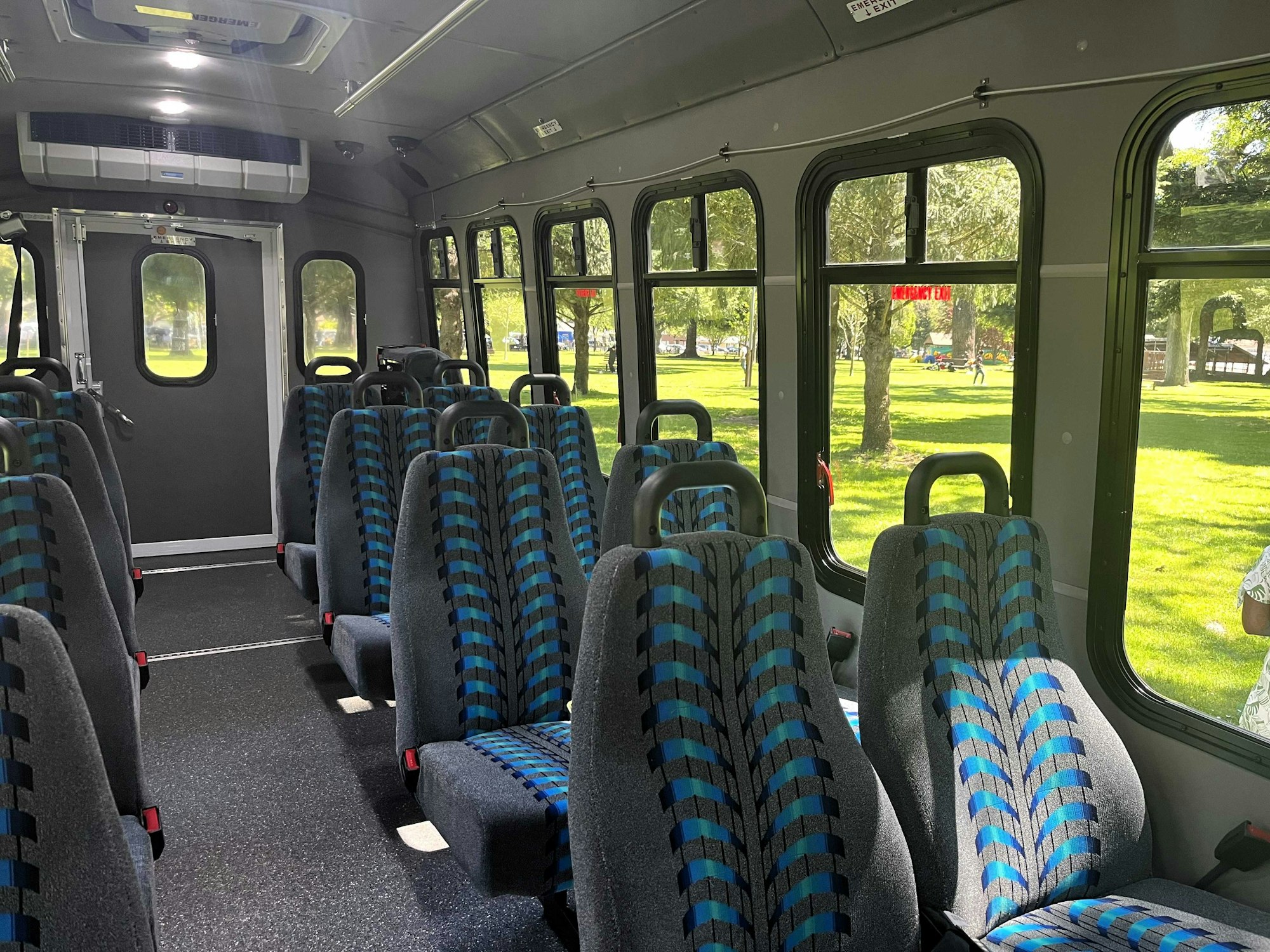 The image shows the interior of a bus, featuring rows of patterned seats and windows with a green park view outside.