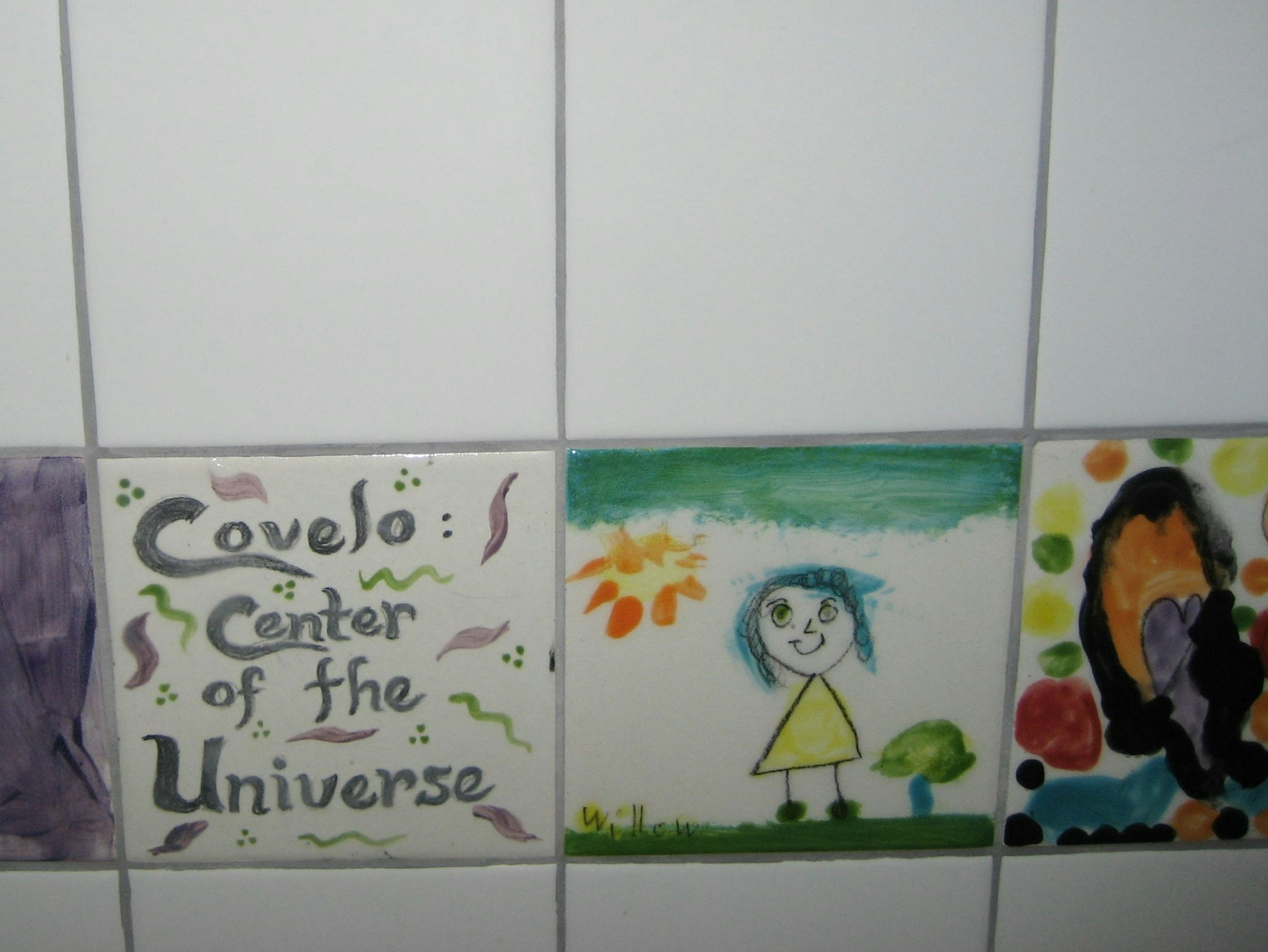 The image shows decorative tiles featuring text about "Covelo: Center of the Universe" and a child's drawing of a girl with blue hair.