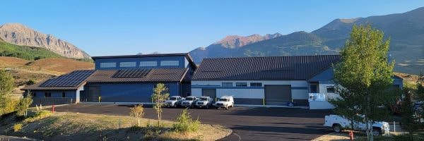 A modern building with solar panels, parking lot, and mountains in the background.