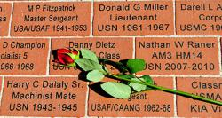 A red rose on a brick wall with inscribed names, suggesting a memorial or tribute to military personnel.