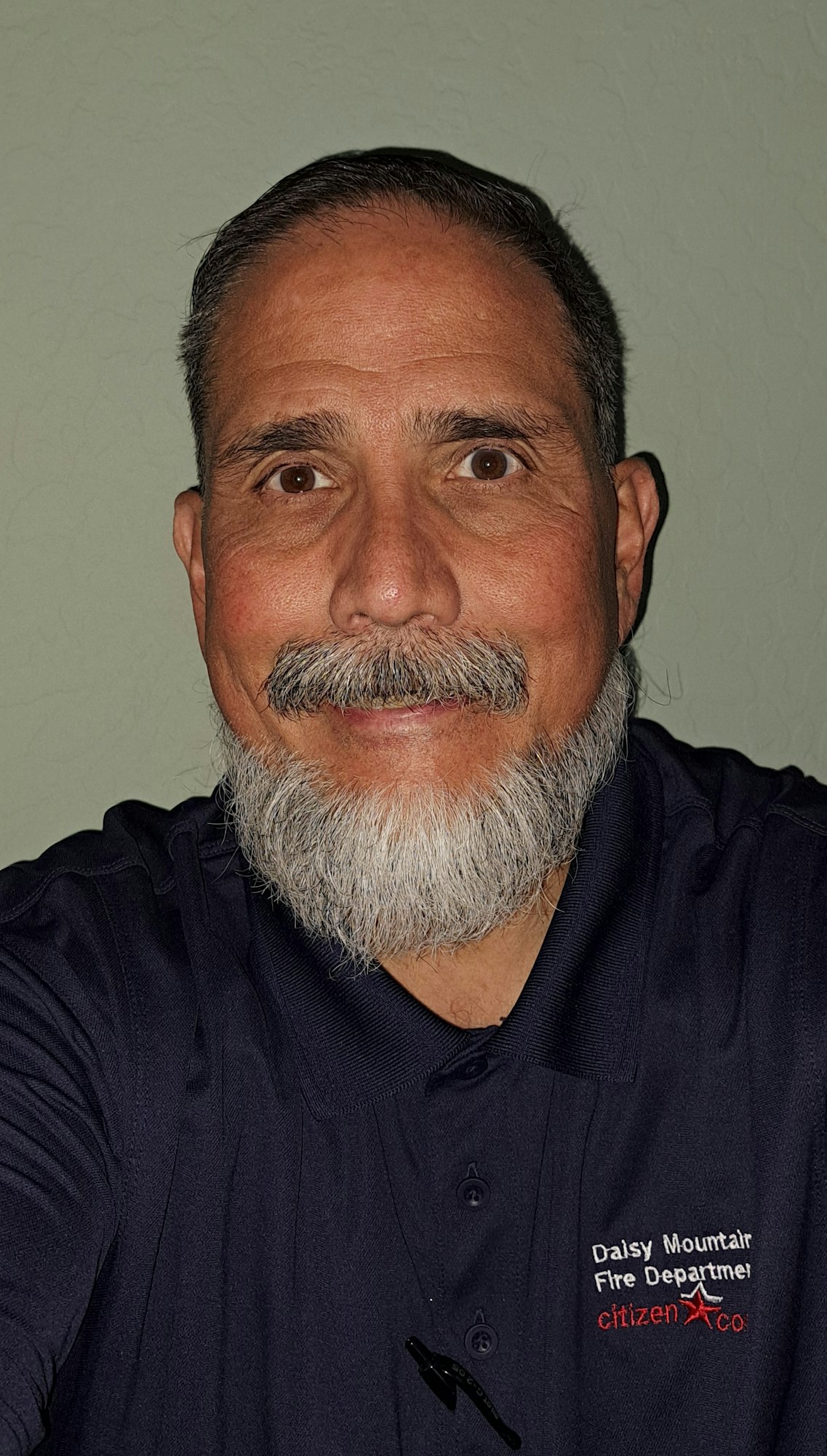 A person with a beard wearing a "Daisy Mountain Fire Department" shirt, smiling at the camera.