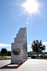 A sundial sculpture under a bright sun in a clear blue sky.