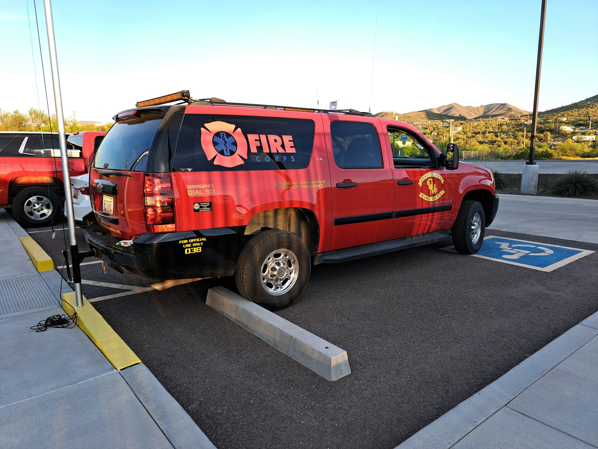 A red fire corps SUV parked over a handicapped spot with surrounding scenic hills.