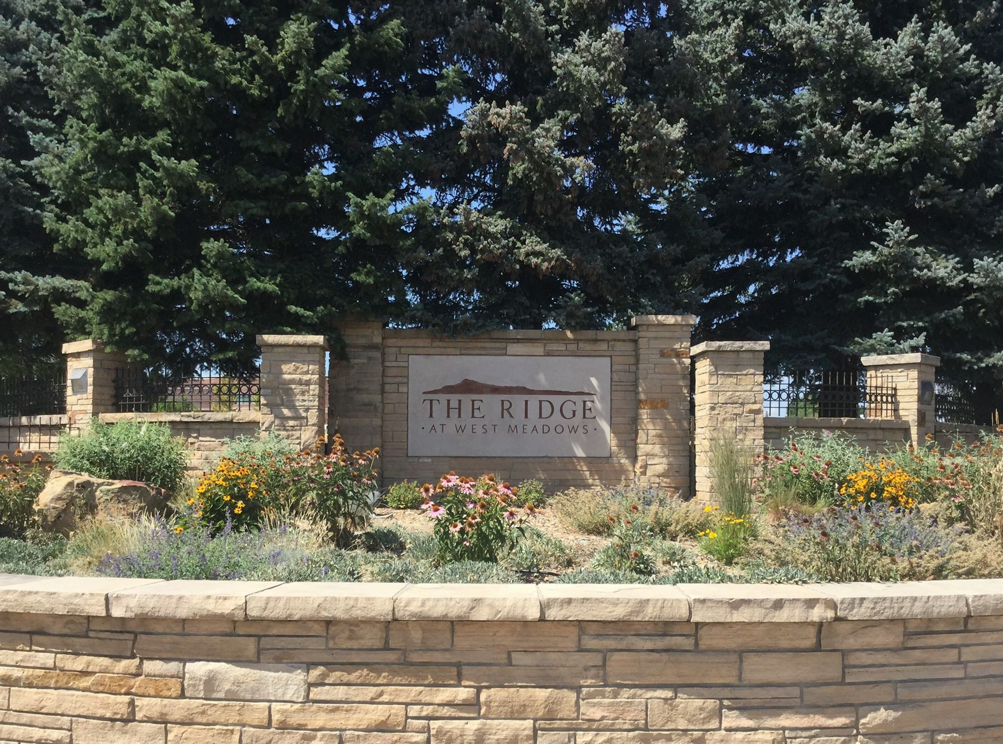 A stone sign for "The Ridge at West Meadows" surrounded by trees and landscaped flowers.