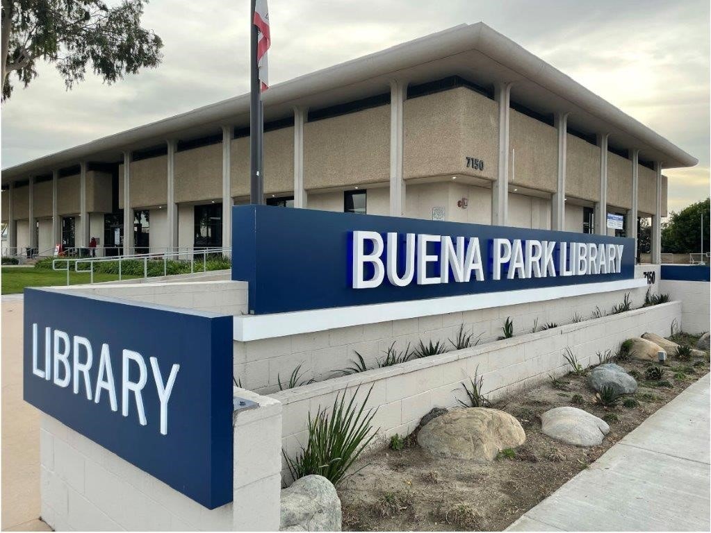 Modern building with a sign reading "Buena Park Library," featuring a landscaped area with rocks and plants.