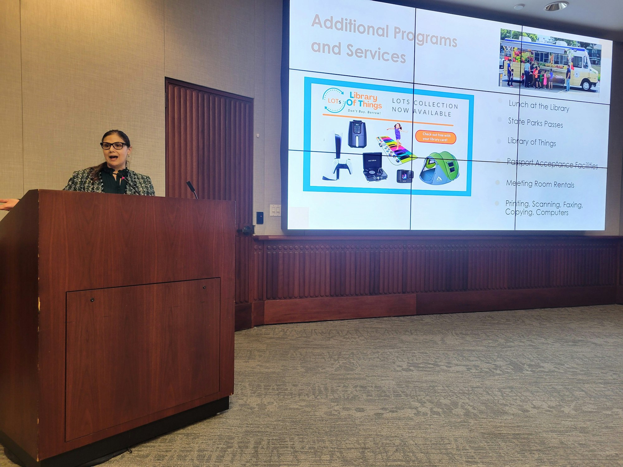 A person is presenting a slide about library programs and services, including a "Library of Things" collection and various community offerings.