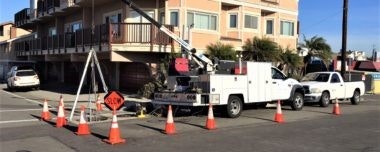 Utility work scene with trucks, cones, and workers at an intersection near a building.