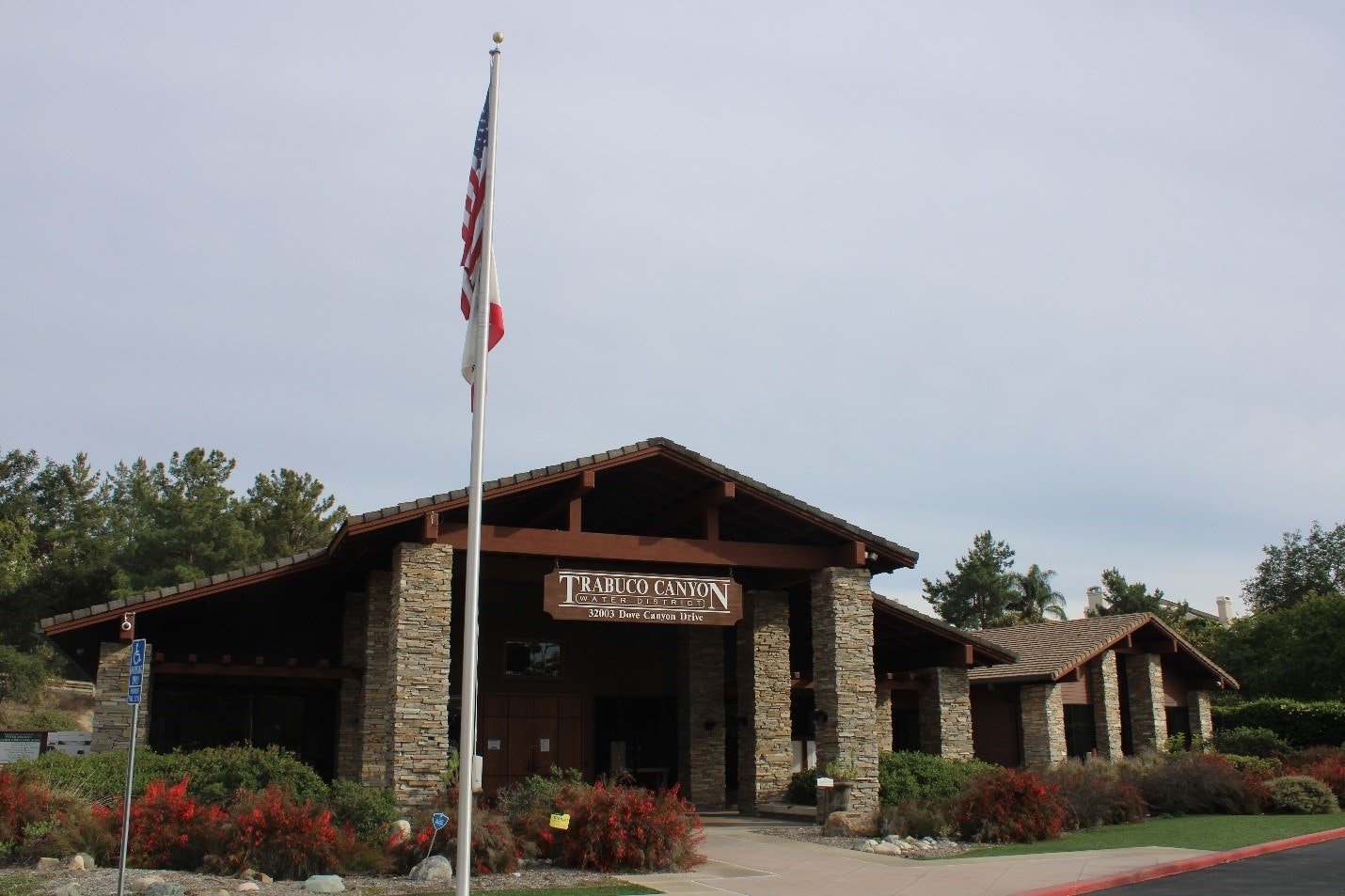 A stone building with a sign reading "Trabuco Canyon Water District," surrounded by greenery and a flagpole with the American flag.