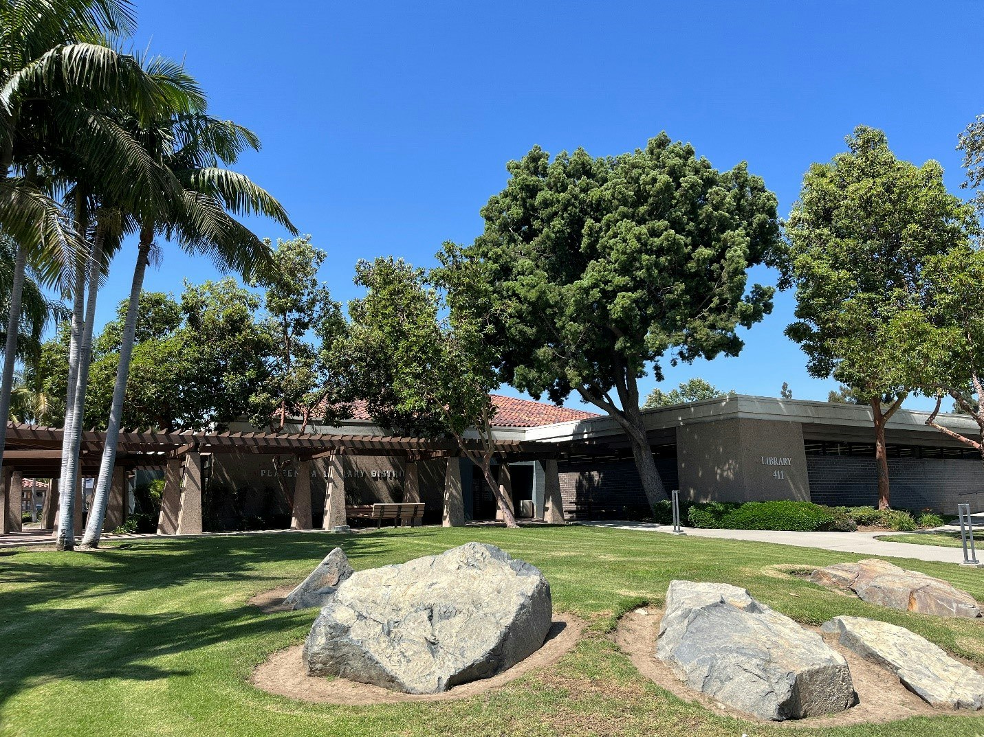 A library building with trees and rocks in the foreground, under a clear blue sky.