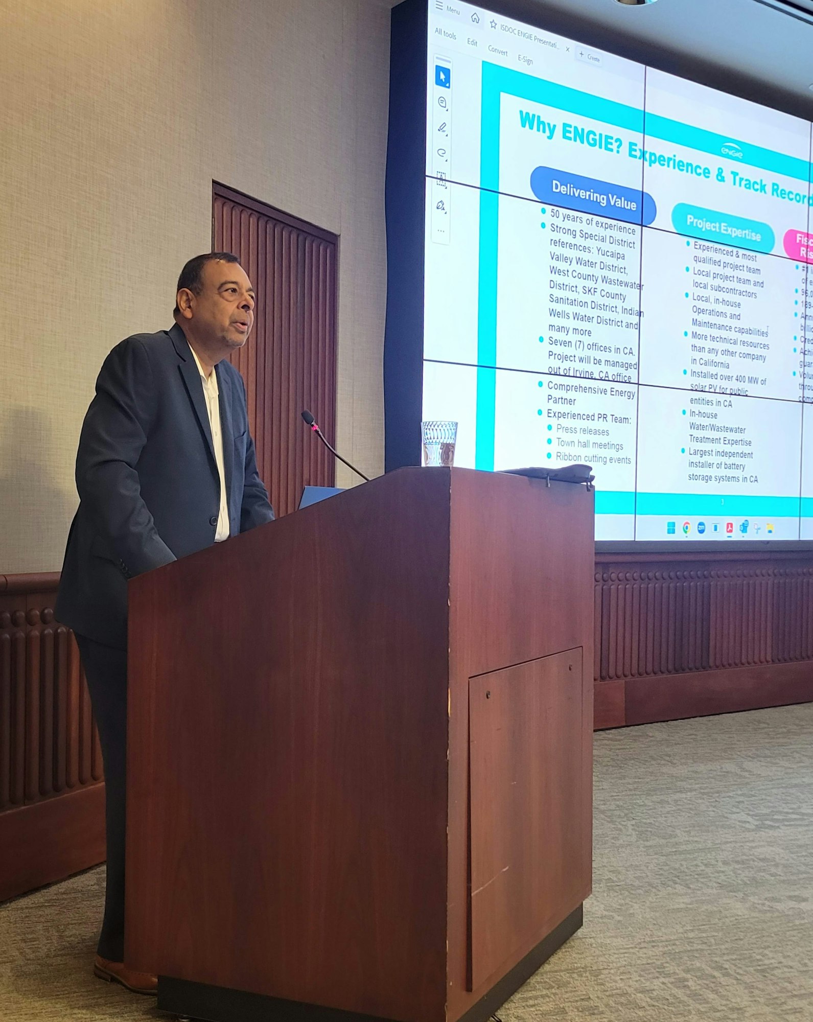 A person in a suit speaks at a podium, with a presentation titled "Why ENGIE?" displayed on a large screen behind them.
