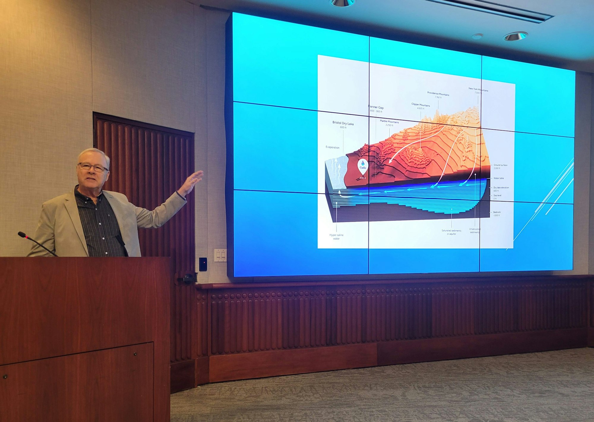 A presenter gesturing at a geologic cross-sectional diagram during a lecture.