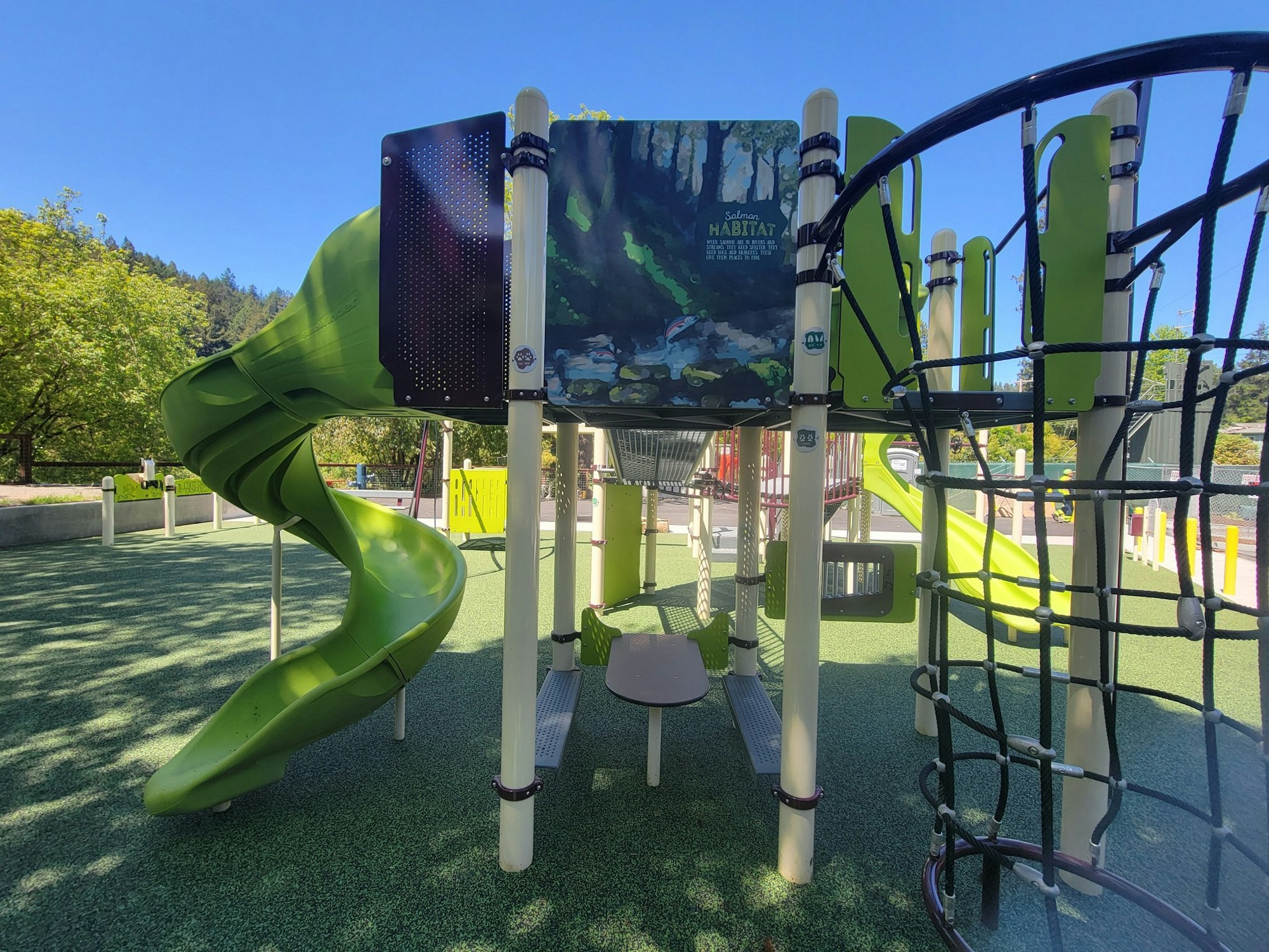 A playground with a green spiral slide, climbing nets, and educational panels.